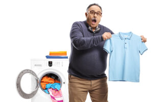 Surprised mature man holding a shrunken t-shirt in front of a washing machine