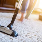 Woman using a vacuum cleaner while cleaning carpet in the house.